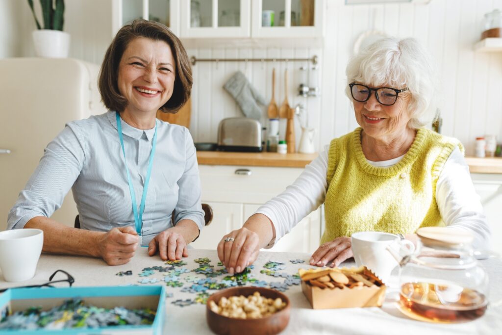 Two,Cheerful,Ladies,Playing,Puzzle,Together,At,Kitchen,Table,,Mature